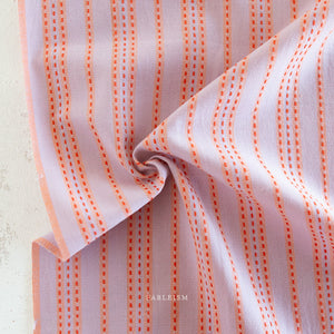 Close up of lavender woven cotton with an orange stitched stripe on a white background.