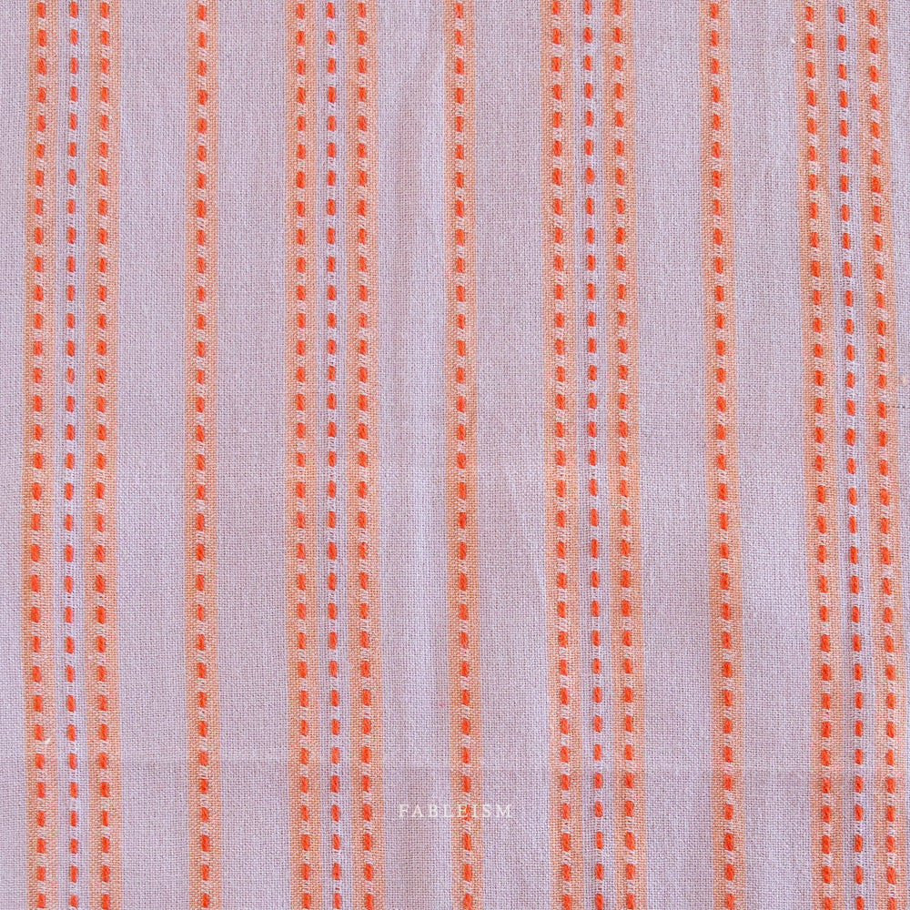 Close up of lavender woven cotton with an orange stitched stripe on a white background.
