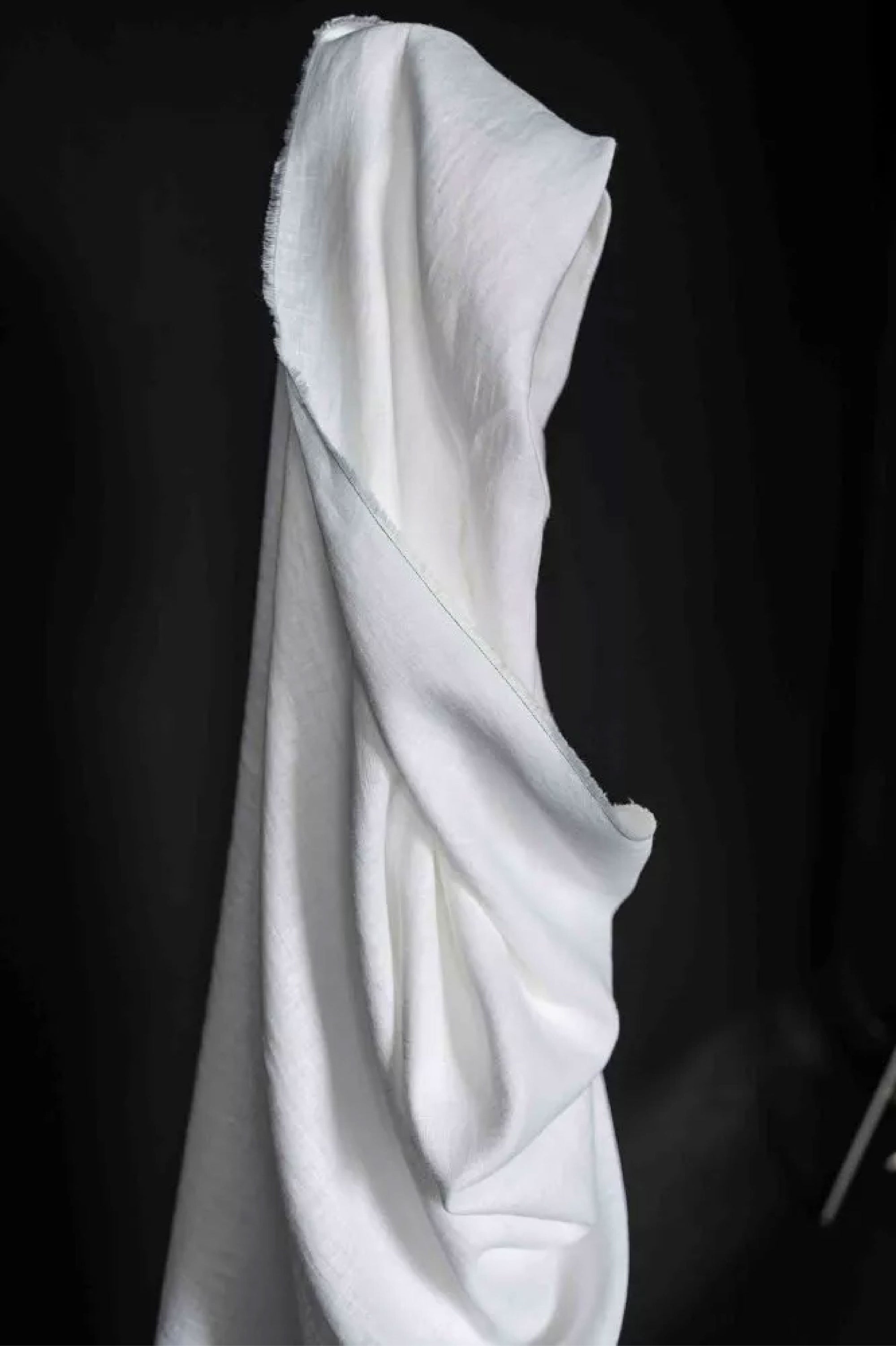 A roll of European laundered linen in pure white on a dark grey background.