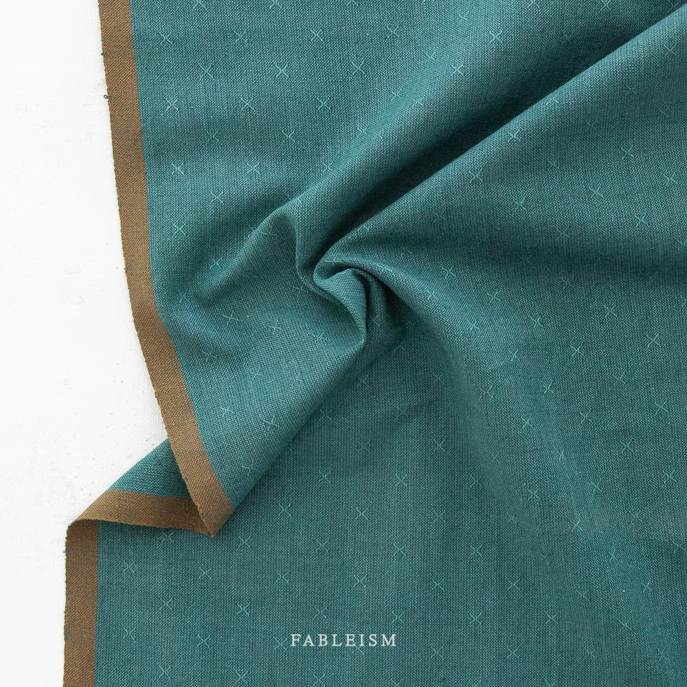 Teal fabric with a woven x pattern and brown selvage, featuring the brand 'Fableism'.