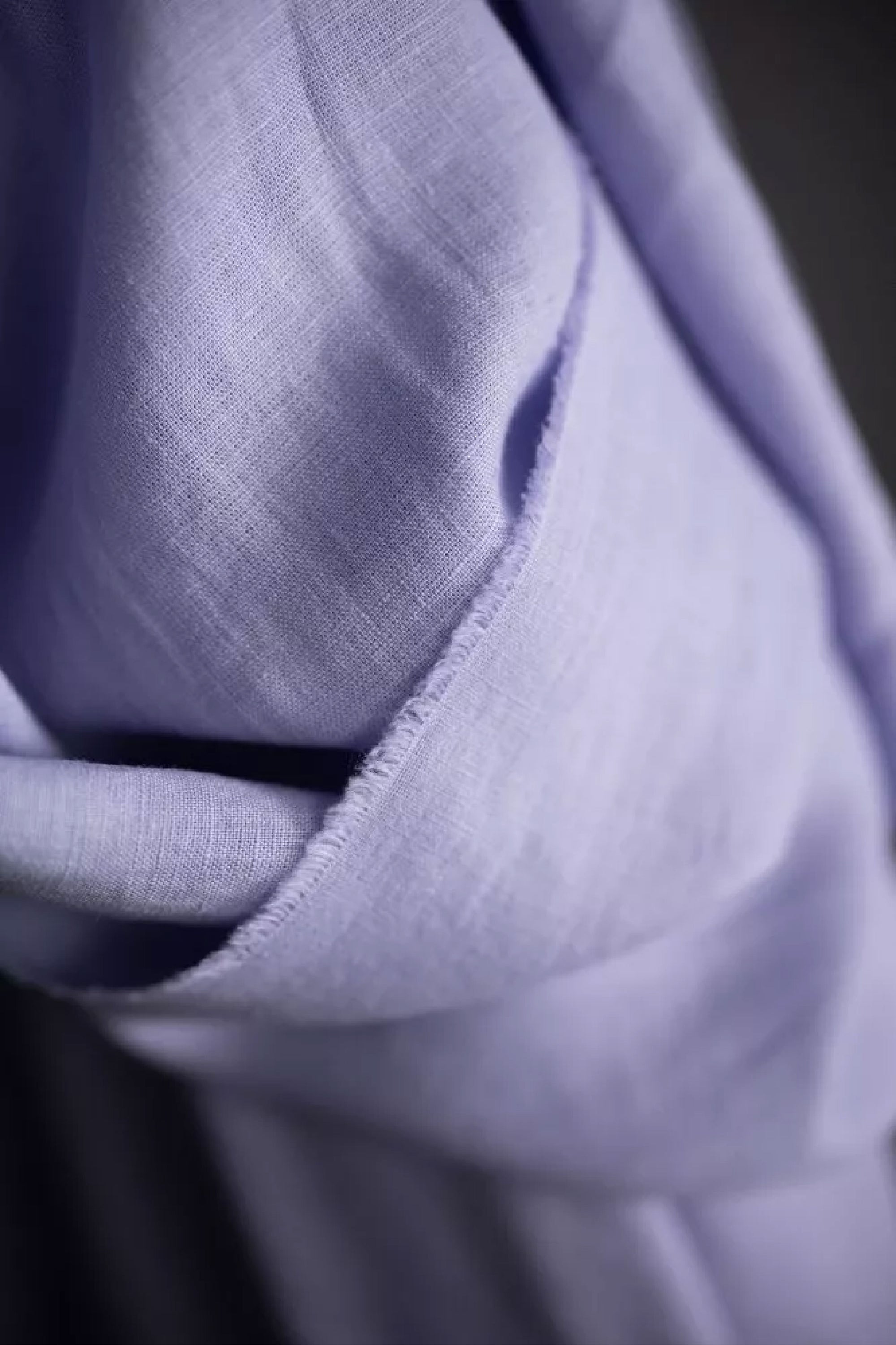 a roll of European laundered linen in soft lilac, on a dark grey background.