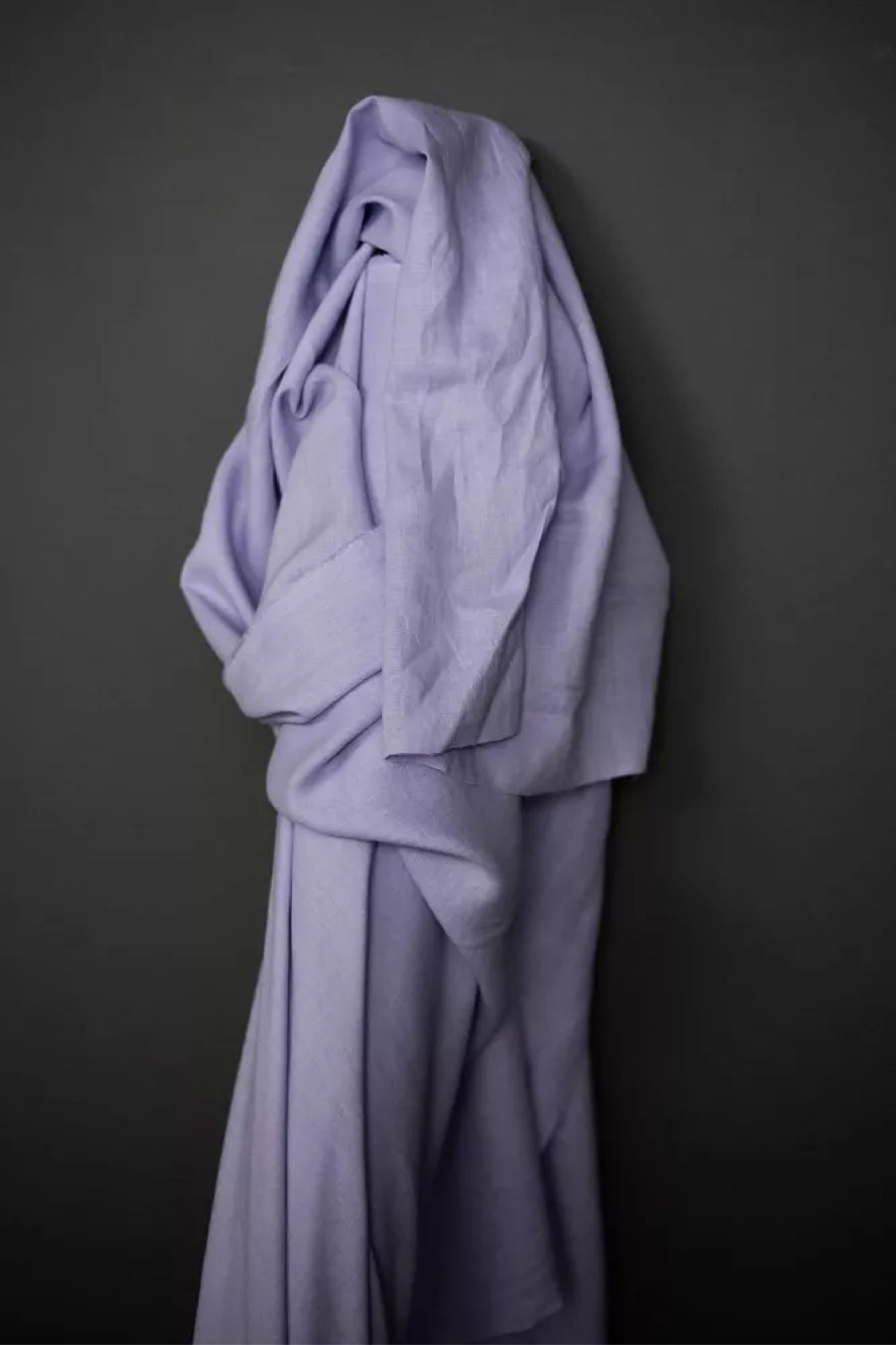 a roll of European laundered linen in soft lilac, on a dark grey background.