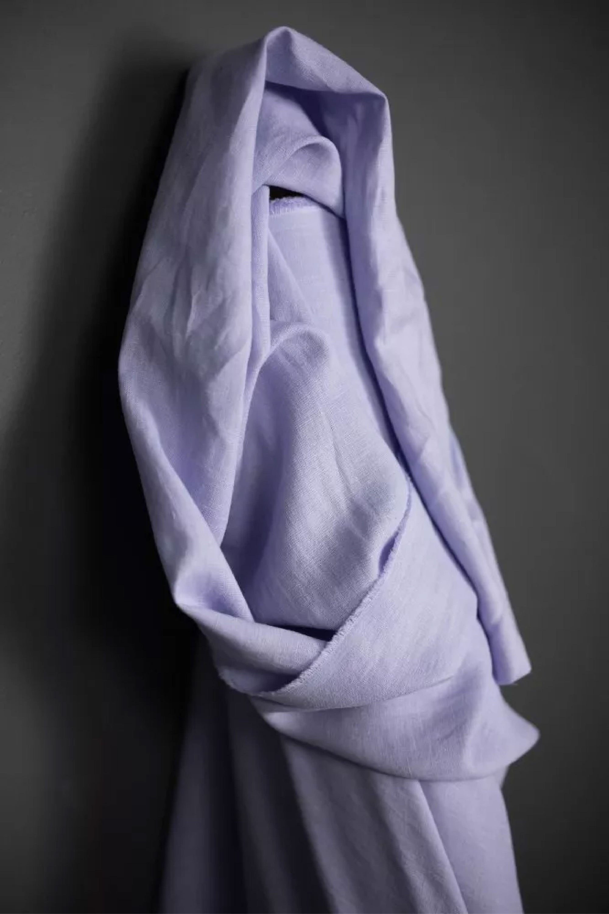 a roll of European laundered linen in soft lilac, on a dark grey background.
