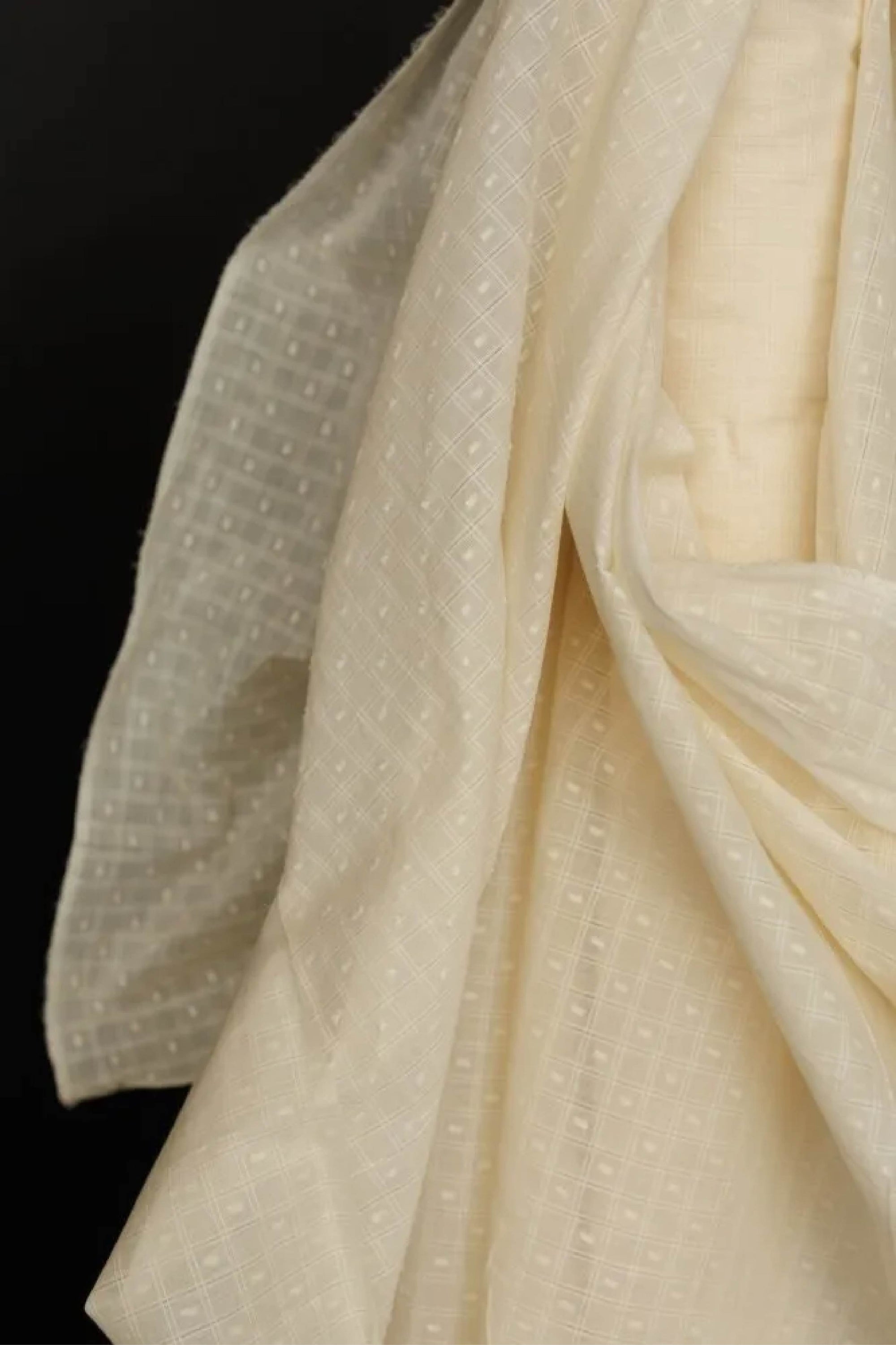 A close up of  draped natural Indian Cotton check in a off-white color on a dark grey background.