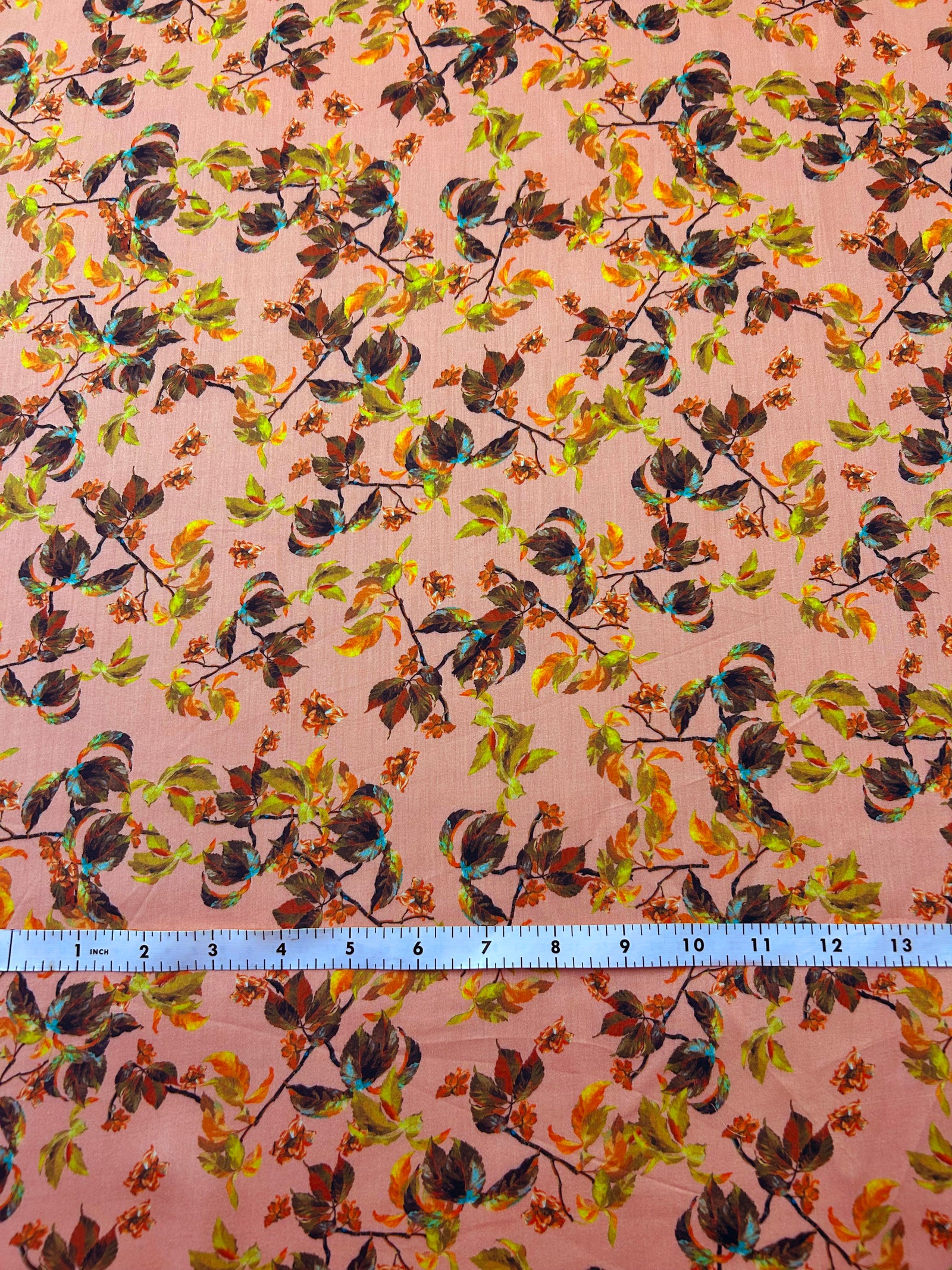Leafy pattern with green, orange, and brown leaves on a peach background with a ruler at the bottom for scale.
