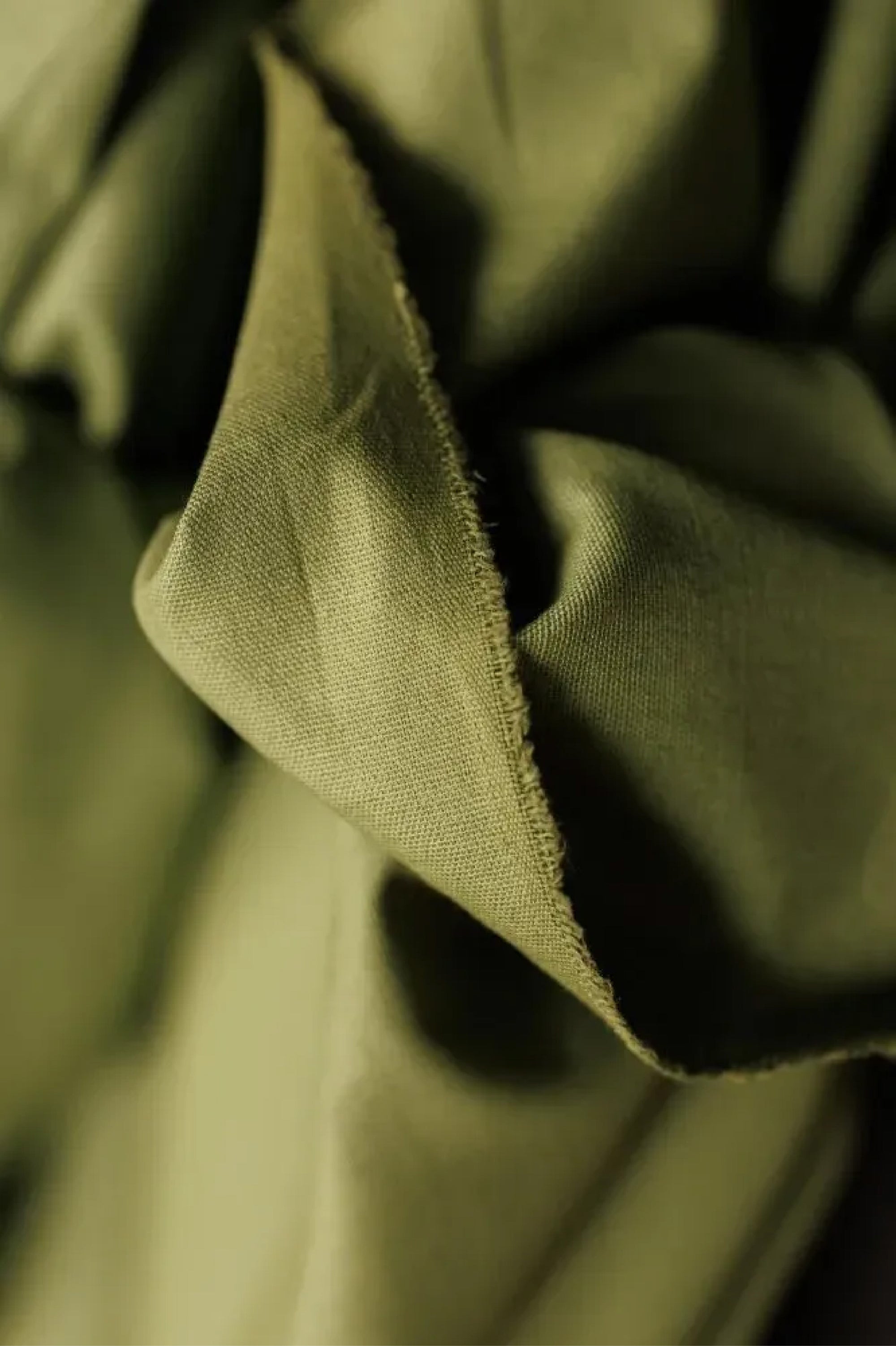 Close up of soft cotton canvas fabric in a classic leafy green color with a matte finish on a dark grey background.