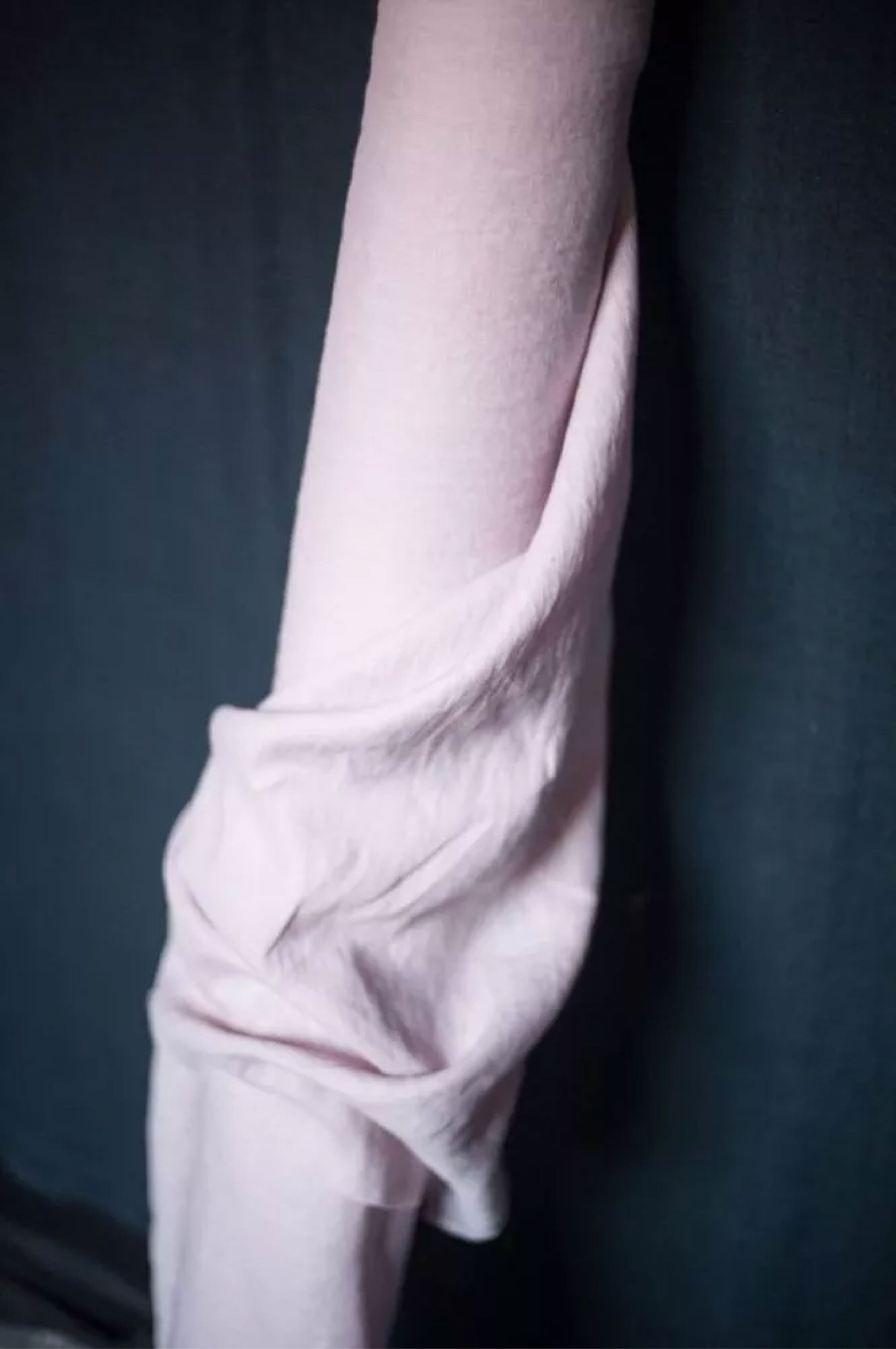 A roll of European laundered linen in a soft chalky pink color on a dark grey background.