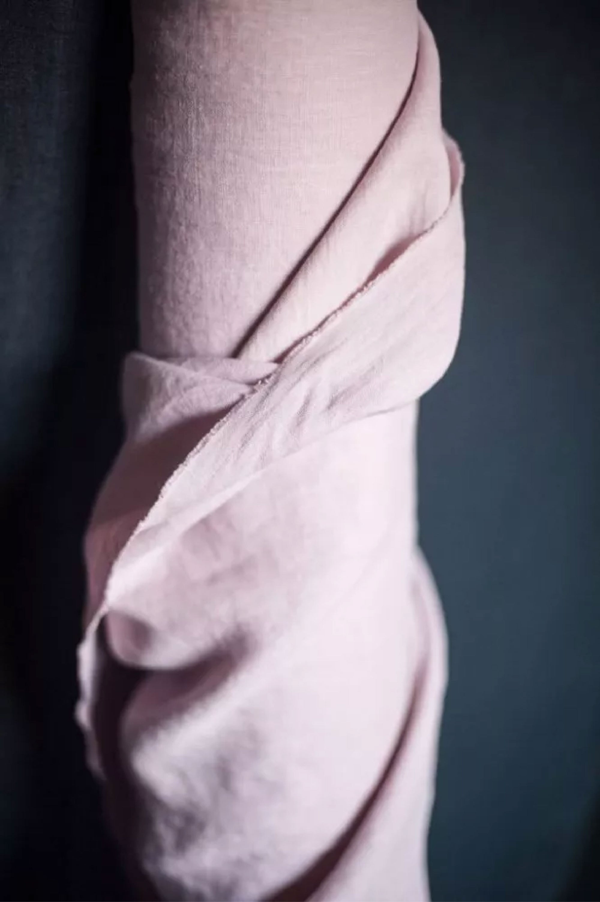 A roll of European laundered linen in a soft chalky pink color on a dark grey background.