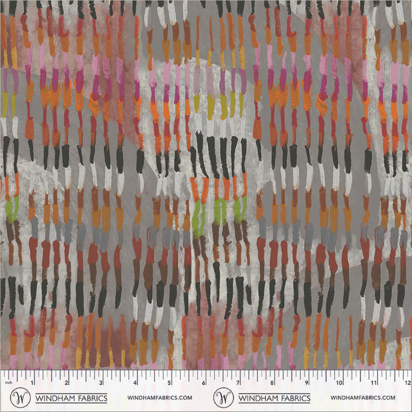 A close-up of a fabric pattern by Windham Fabrics featuring vertical brushstroke-like dabs in pink, orange, yellow, green, black, brown, and white over a mottled gray background, with a printed ruler scale along the bottom edge.