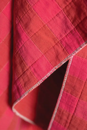 Close-up of a quilted cotton jacquard fabric with a checkered pattern on red and fuchsia.