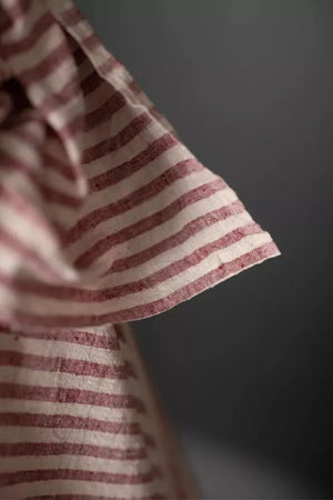 close up of a handloomed candy stripe of dusty red and natural with a loose weave and a washed out slubby texture fabric on a dark grey background.