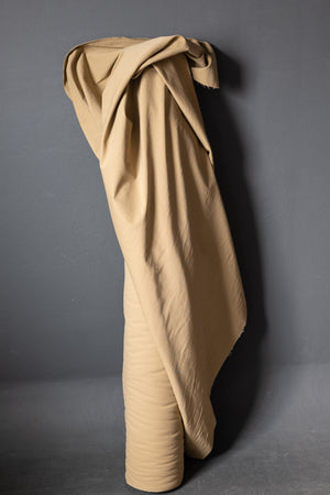 Roll of cotton sanded twill fabric in a dark beige color Sand. Standing on a dark grey background.