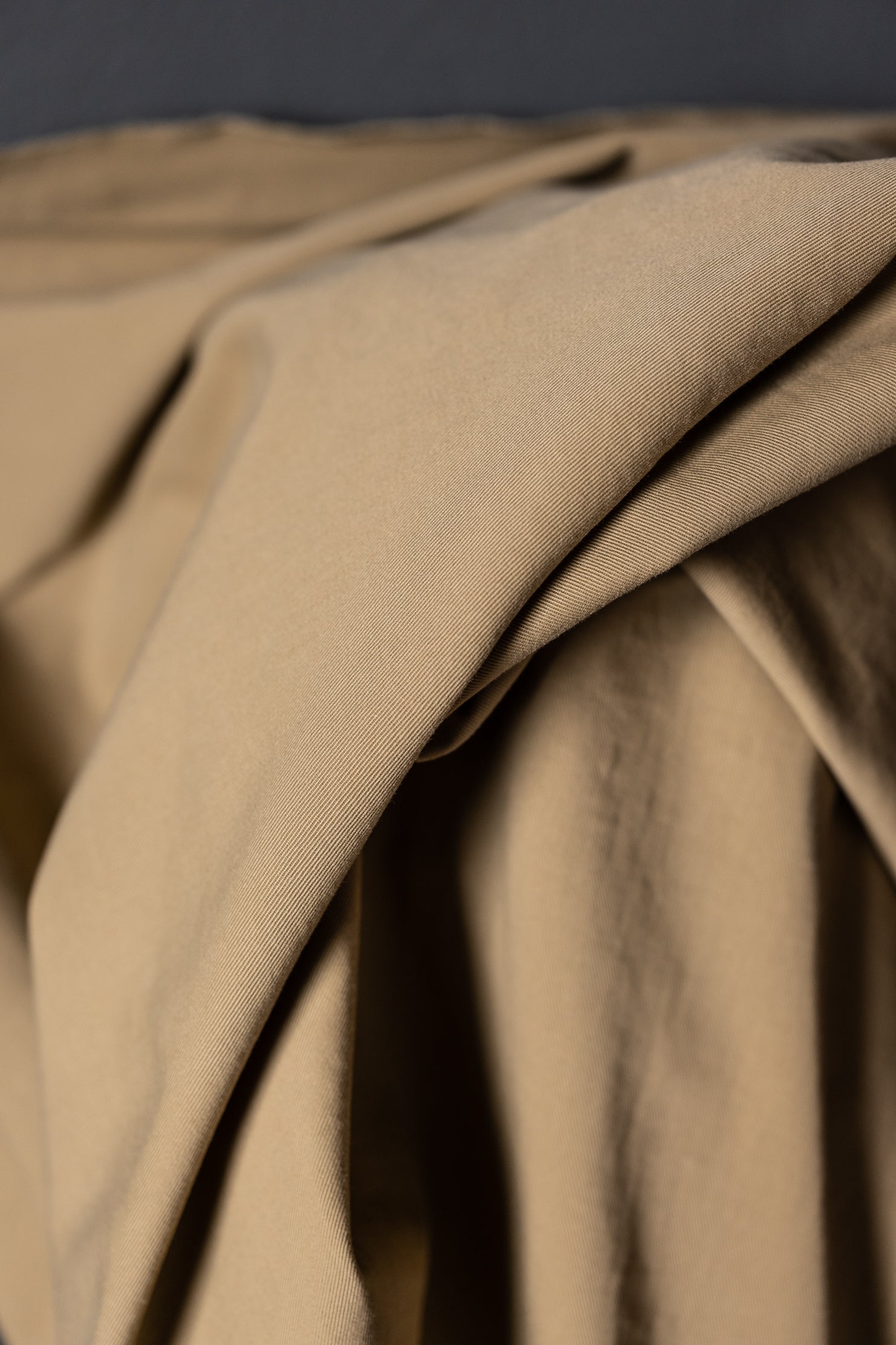 Roll of cotton sanded twill fabric in a dark beige color Sand. Standing on a dark grey background.