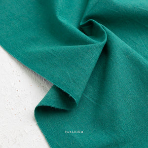 Close-up of teal green fabric with 'Fableism' branding on a light background