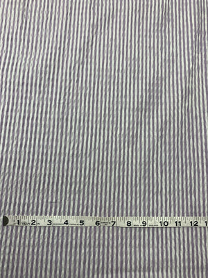 A cotton seersucker fabric in a striped Lilac and White vertically with a measuring tape on top of the fabric.