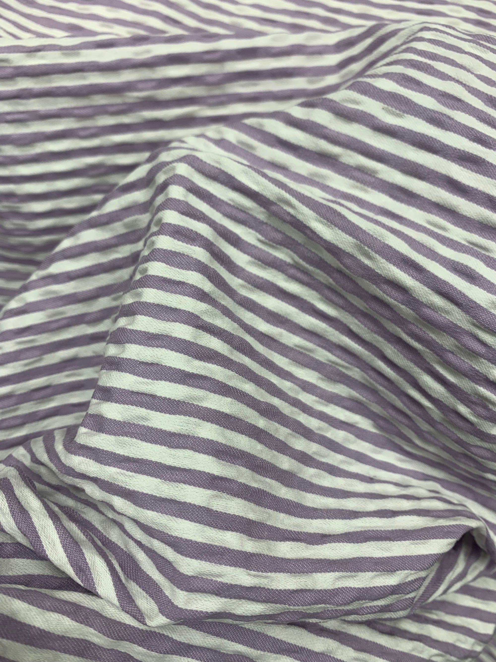 A draped  cotton seersucker fabric in a striped Lilac and White horizontally.