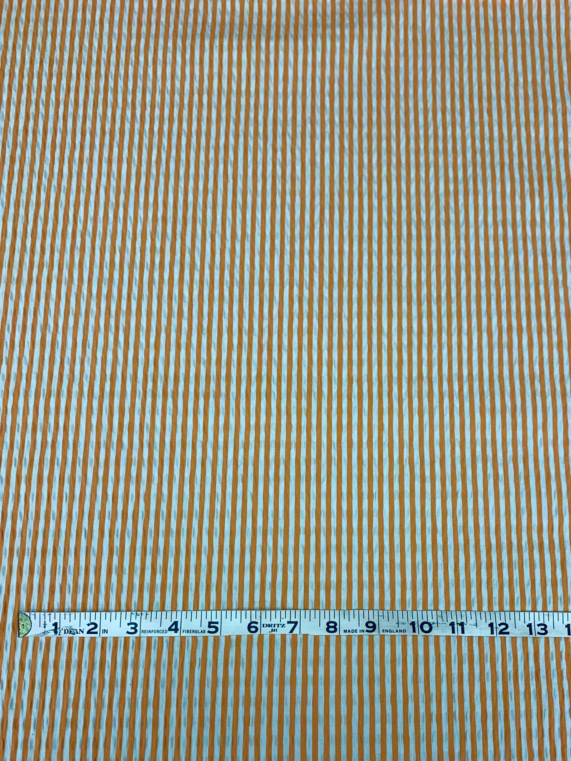 cotton seersucker in a striped Orange and White vertically  with a measuring tape on top of the fabric