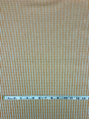 cotton seersucker in a striped Orange and White vertically  with a measuring tape on top of the fabric