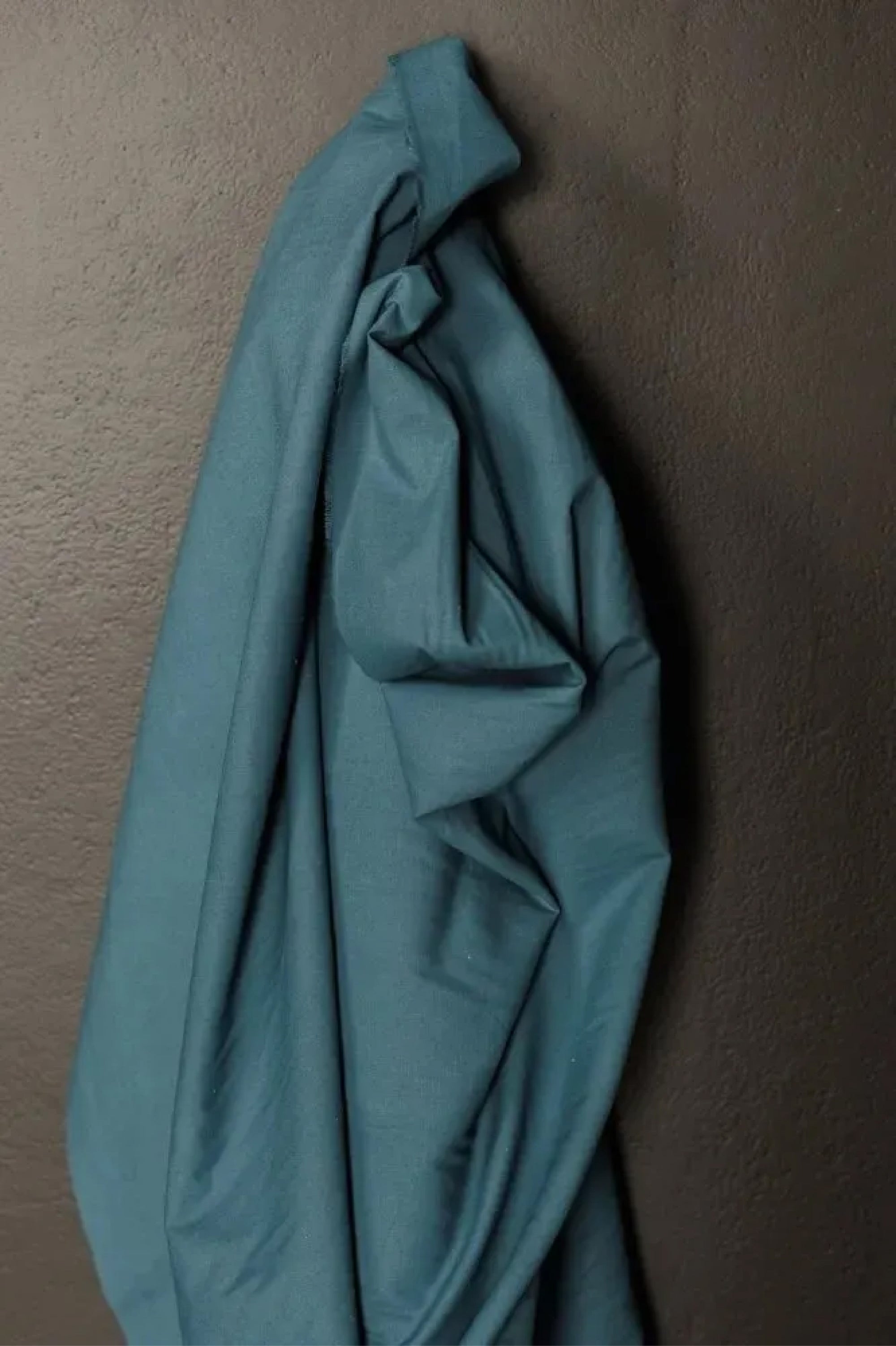 A soft cotton canvas fabric is a teal color with a matte chalky finish, on a dark grey background.