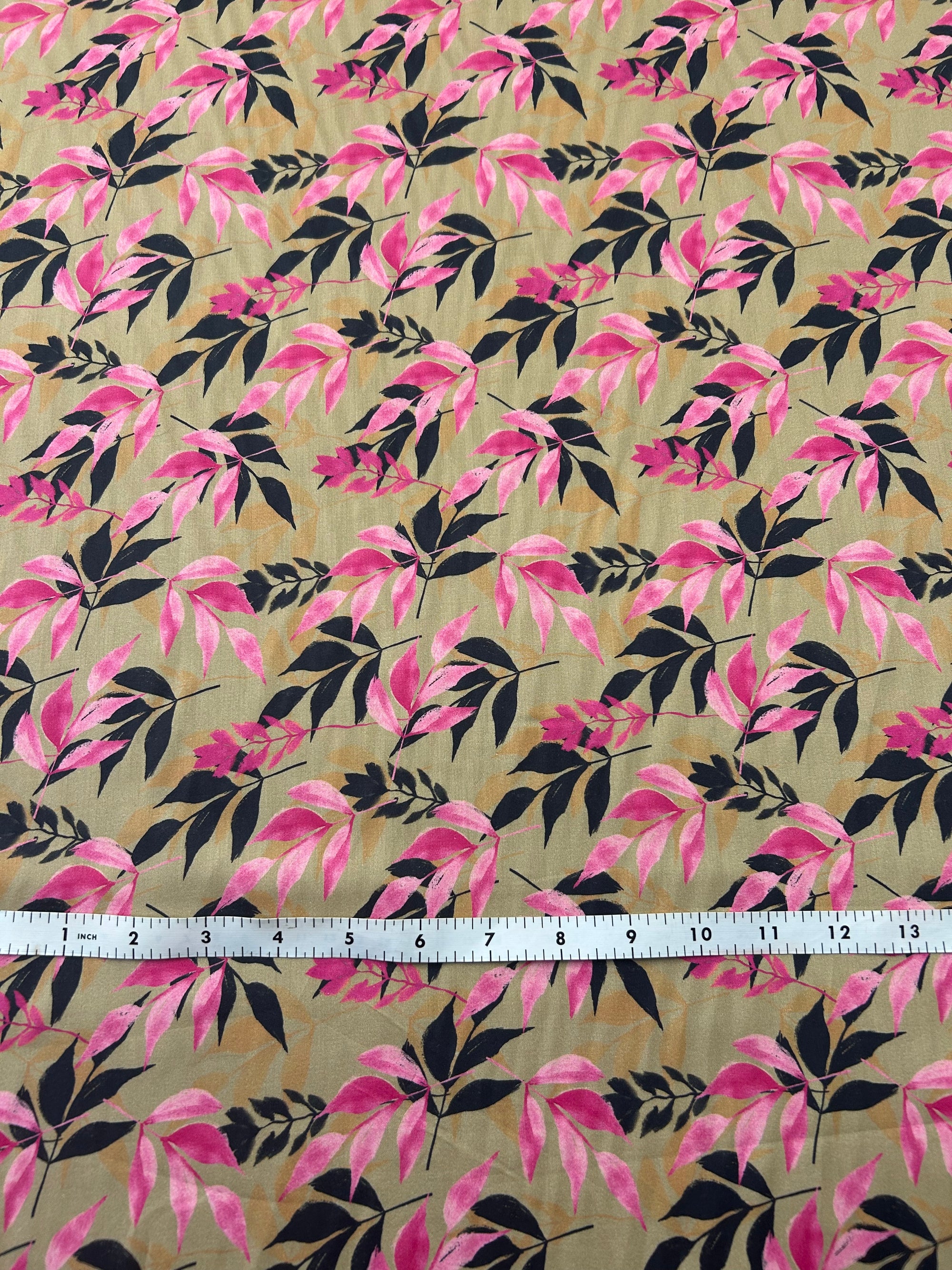 Fabric with pink and a black silhouette leaf pattern on tan background, with a measuring tape on top.
