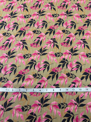 Fabric with pink and a black silhouette leaf pattern on tan background, with a measuring tape on top.