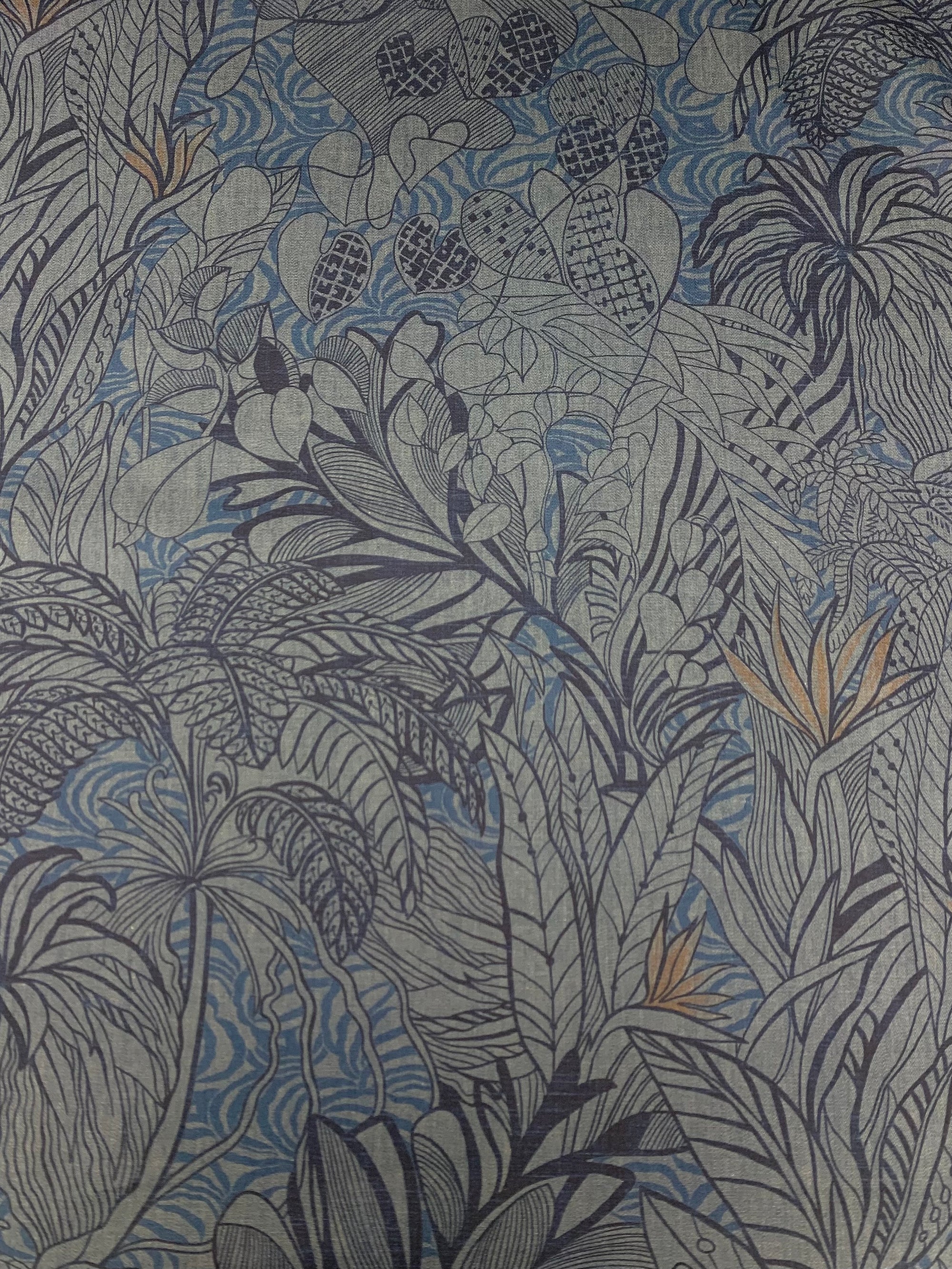 Cotton chambray fabric with a tropical blue print with touches of orange on a denim blue background 