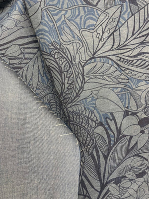 A double sided cotton chambray fabric with a tropical blue print with touches of orange on a denim blue background on one side and a denim blue color on the other.