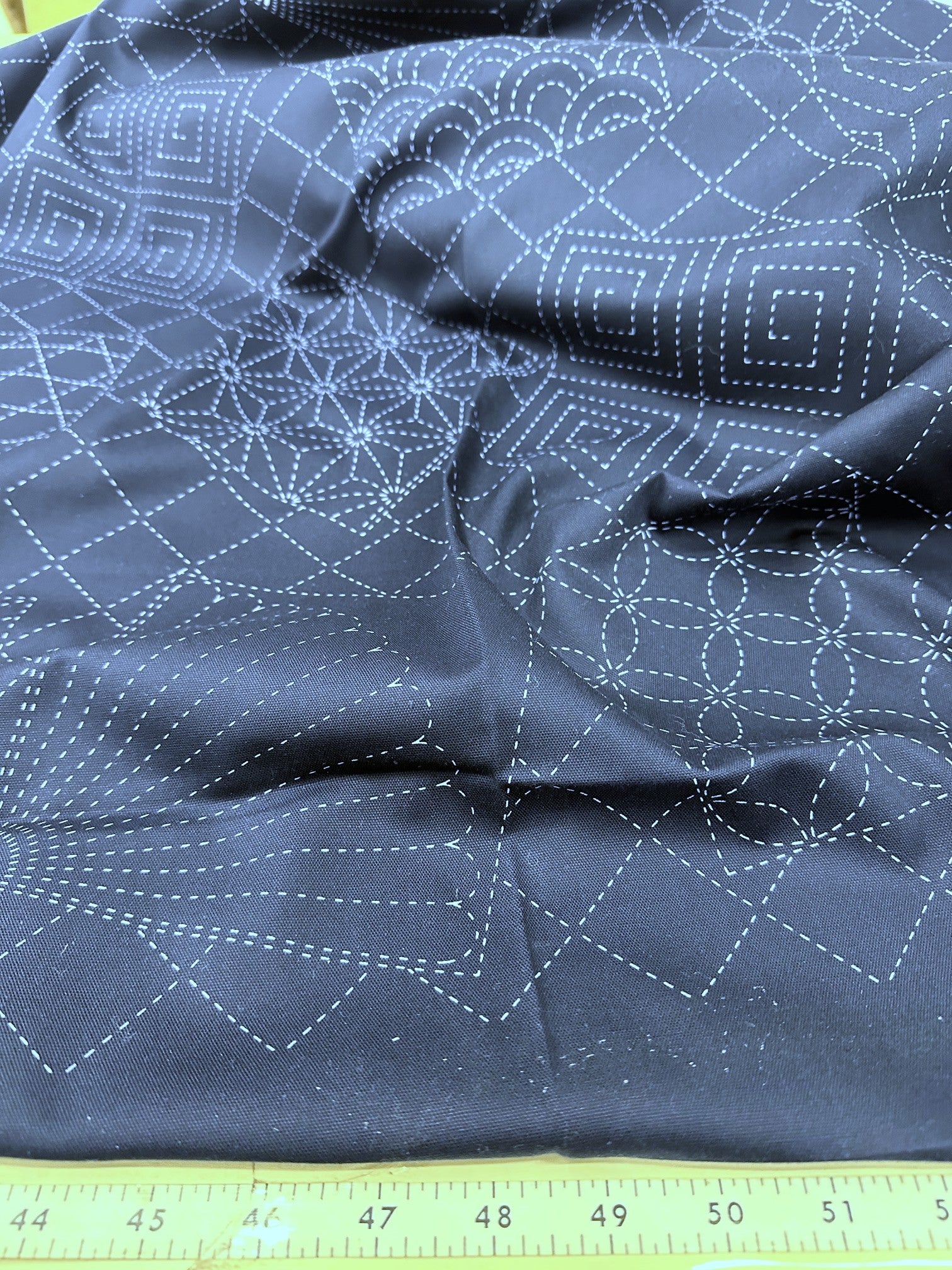 Dark blue fabric with white geometric stitching pattern, measured against a yellow ruler.