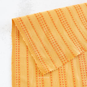 Close-up of orange fabric with red stitching on a white background