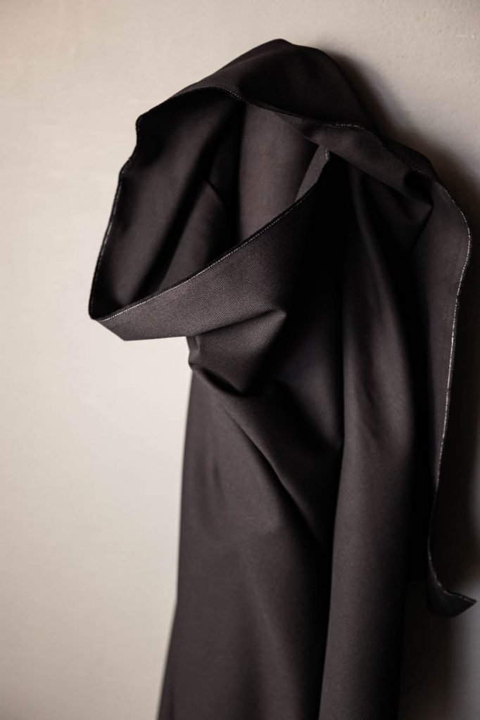 Black cotton canvas fabric standing up against a off white background.