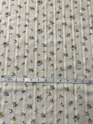 cotton fabric with a vintage blue and mustard floral print with embroidered vertical stripes with a white measuring tape on top.