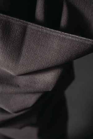 Close up of Cotton canvas fabric is a warm charcoal color. draped over a cylindrical object against a dark background.