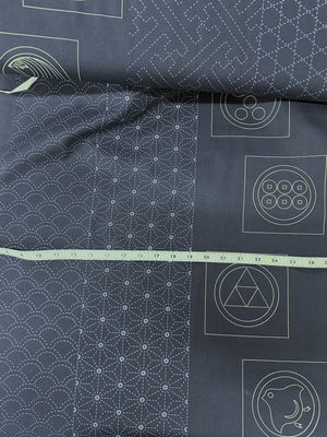 Dark fabric with white sashiko patterns and symbols, with a measuring tape for scale.