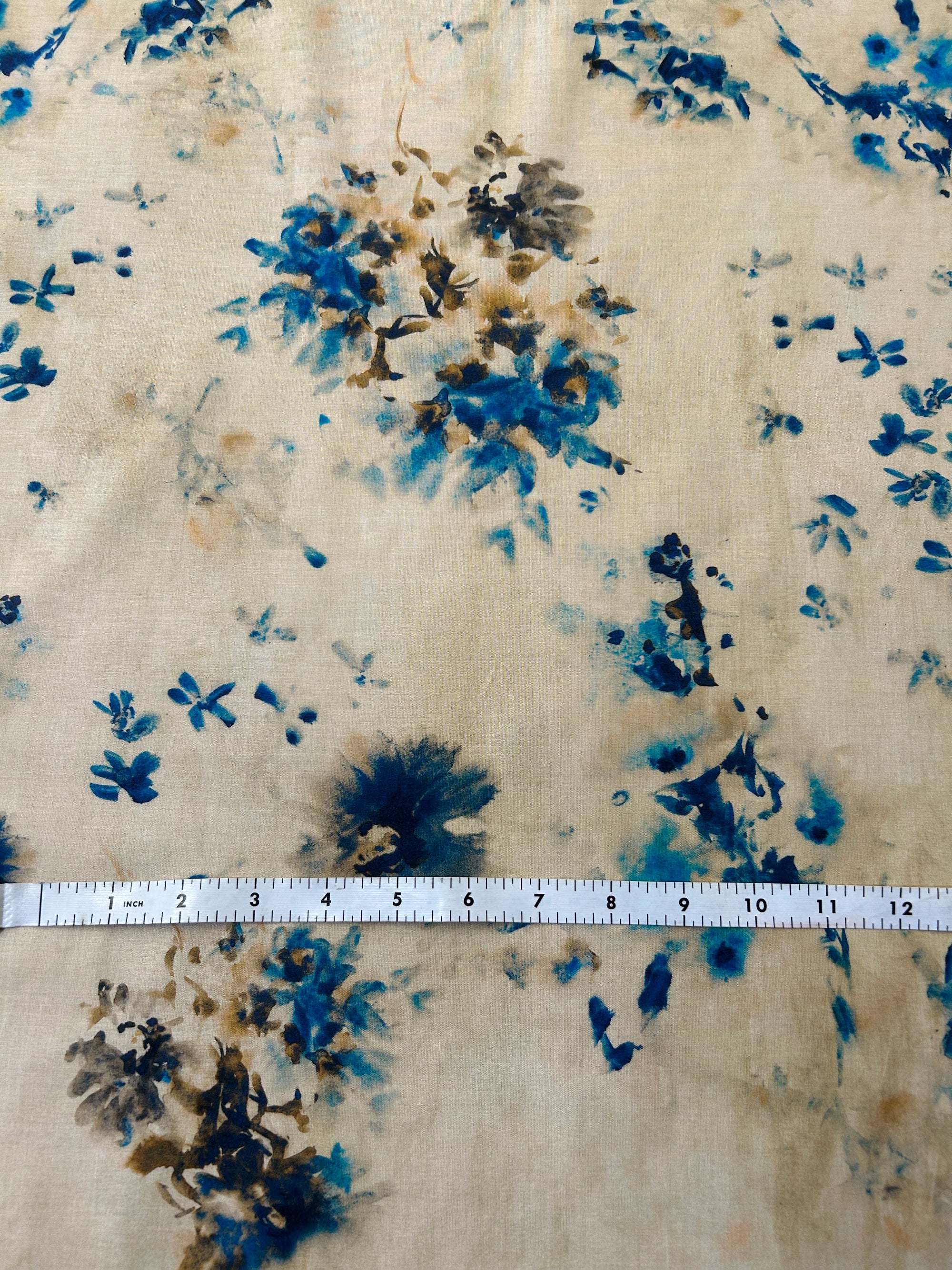 a vibrant print of spashes of blue watercolor florals and a ruler for scale on a beige background