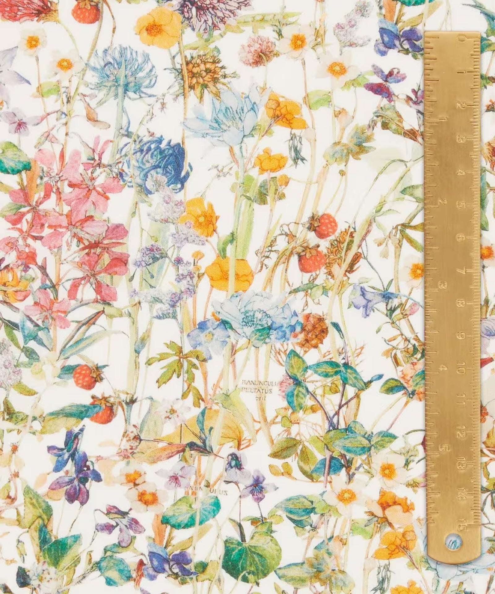 Close up of a soft print of wild flowers of reds, pinks, blues, and yellows with light green foliage on a green background.