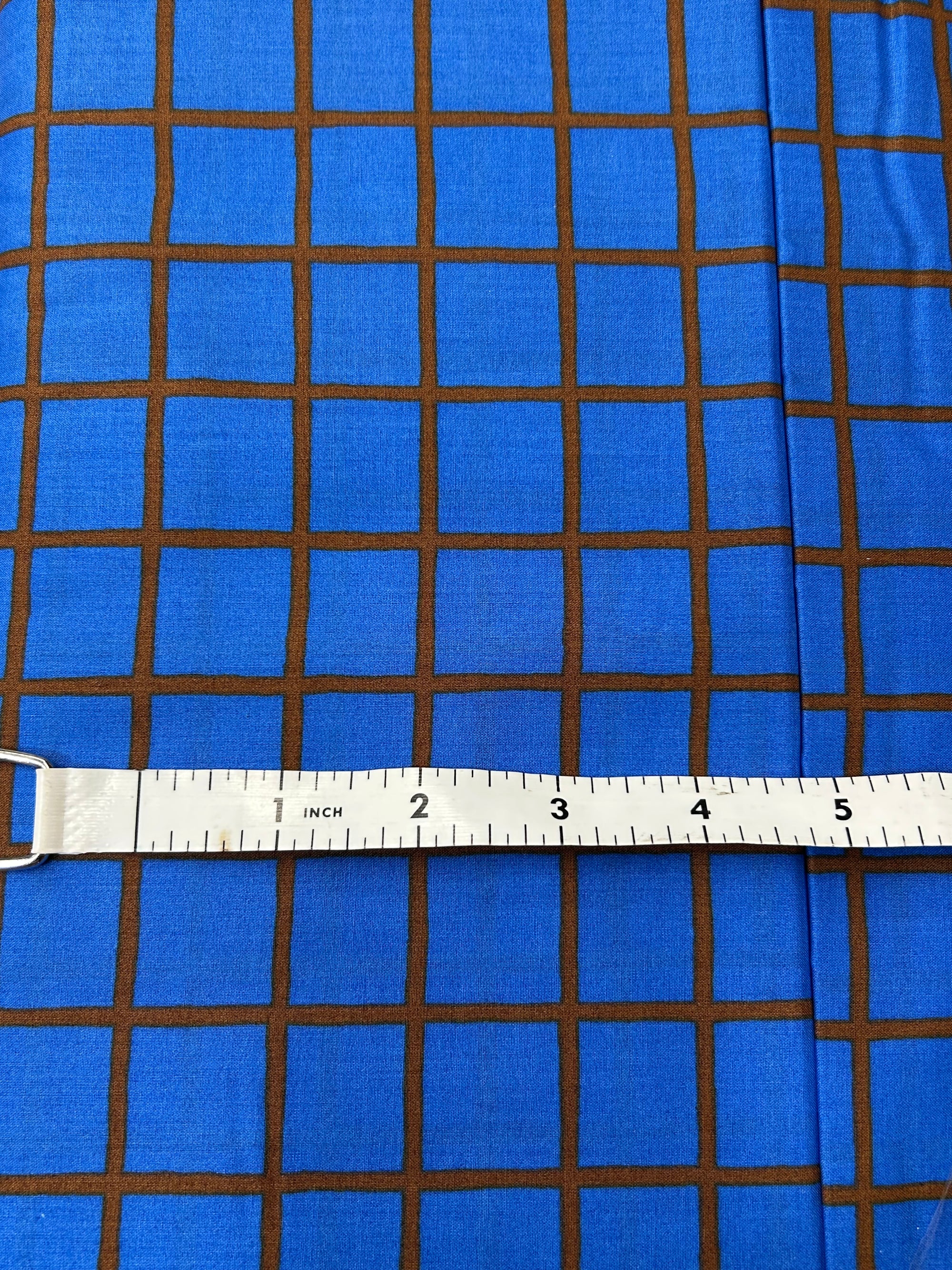 organic cotton lawn in blue with a deep auburn window pane check with measuring tape on top.