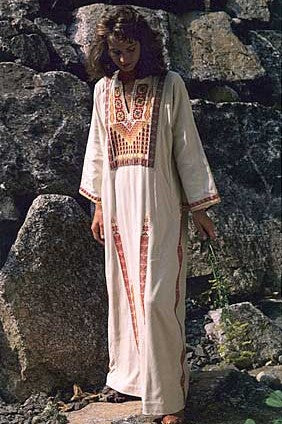 Woman in a white Gaza Dress (thobe) with red embroidery standing by boulders