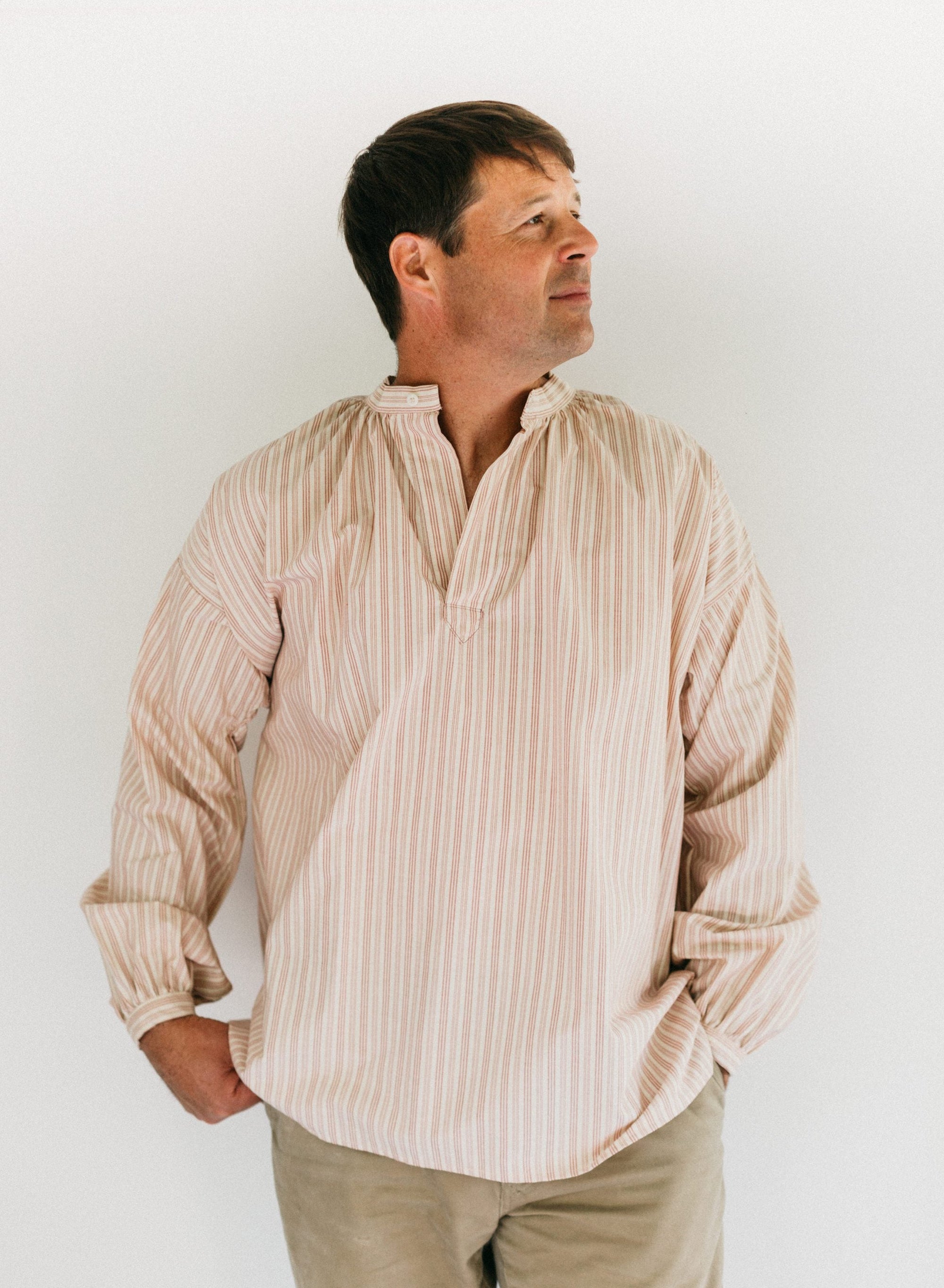 Man wearing striped French Cheesemakers Smock standing in front of white background.