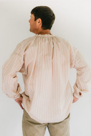 Man wearing striped French Cheesemakers Smock standing in front of white background. His back is turned toward the camera.