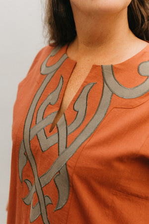 Woman in coral Egyptian Shirt.  Close up of front yoke with neck slit and gray applique.