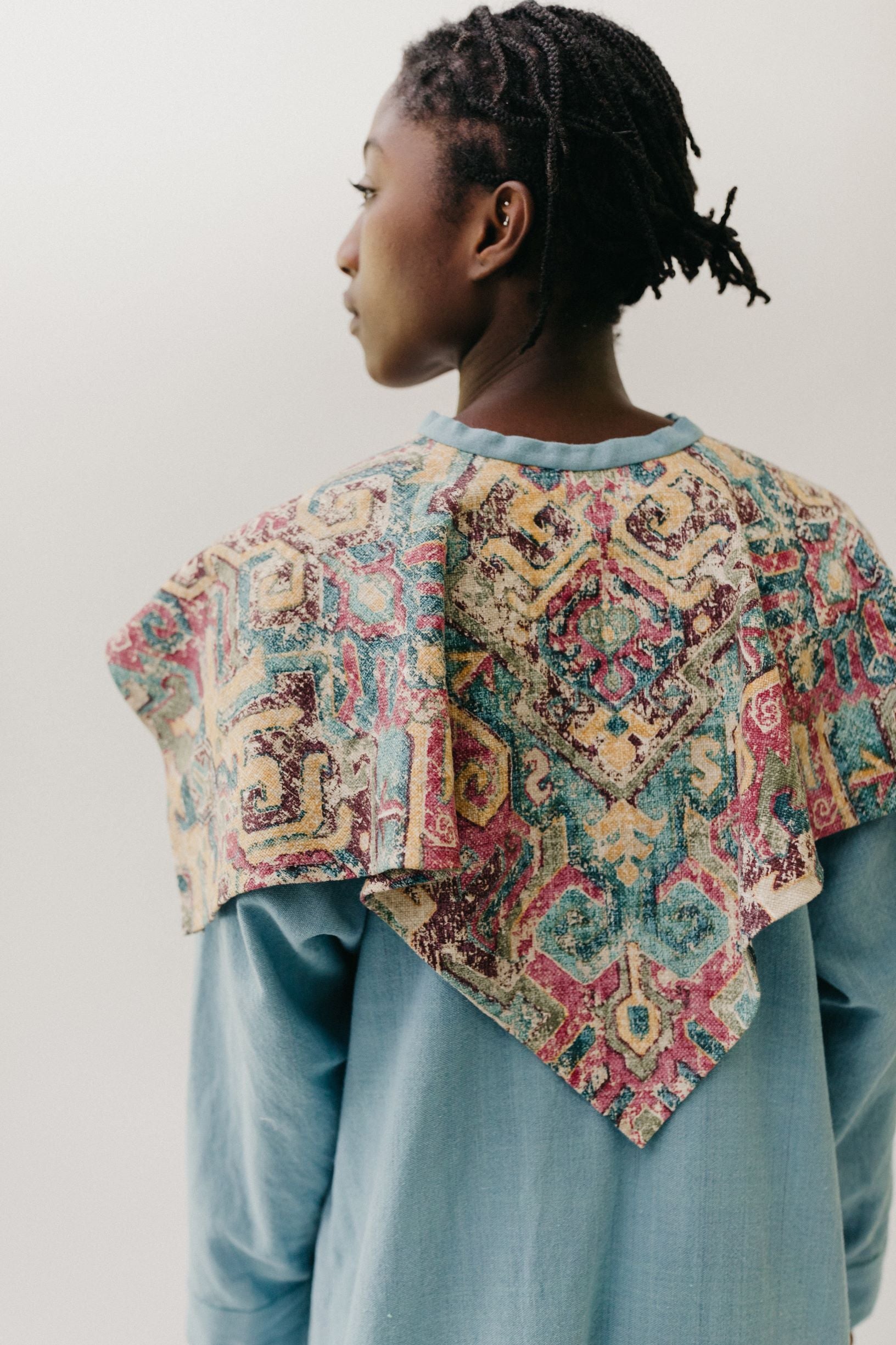 Black woman walking toward camera wearing a long blue dress with an embroidered triangular collar yoke. Close up of back of triangular collar.  On a white background.