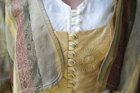 Close up photo of the front of jacket over vest and tunic as under layer.  Closures of vest and jacket are the focus of the photo.
