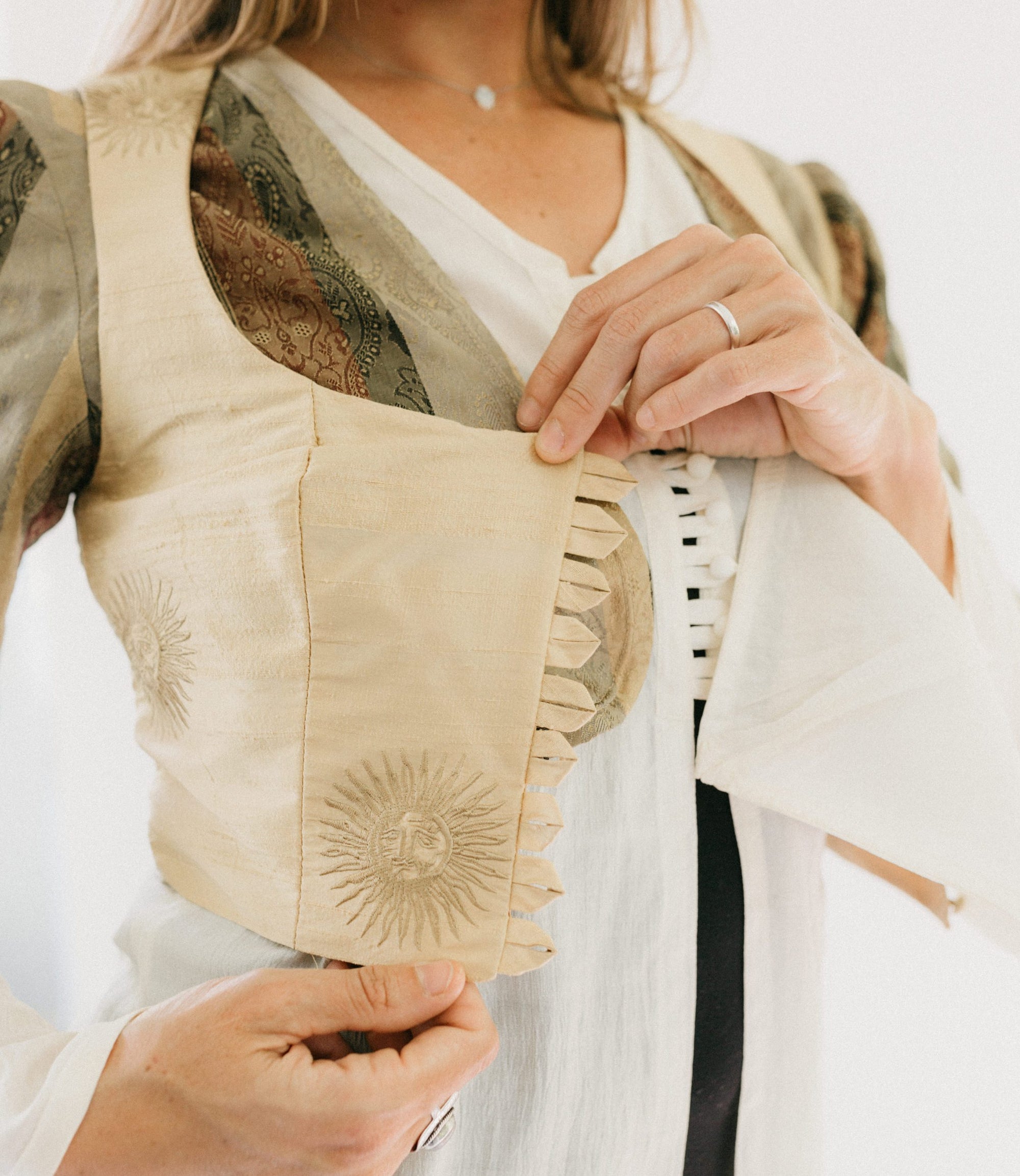 Close up photo of the button loops on the vest.  vest is over the jacket and tunic.  It is unbuttoned and model holds out the closure to show details.