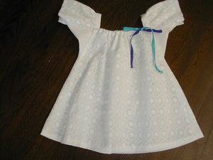 Photo of white eyelet Mexican Baby Dress.  View is from front and dress is laying flat on a wood floor