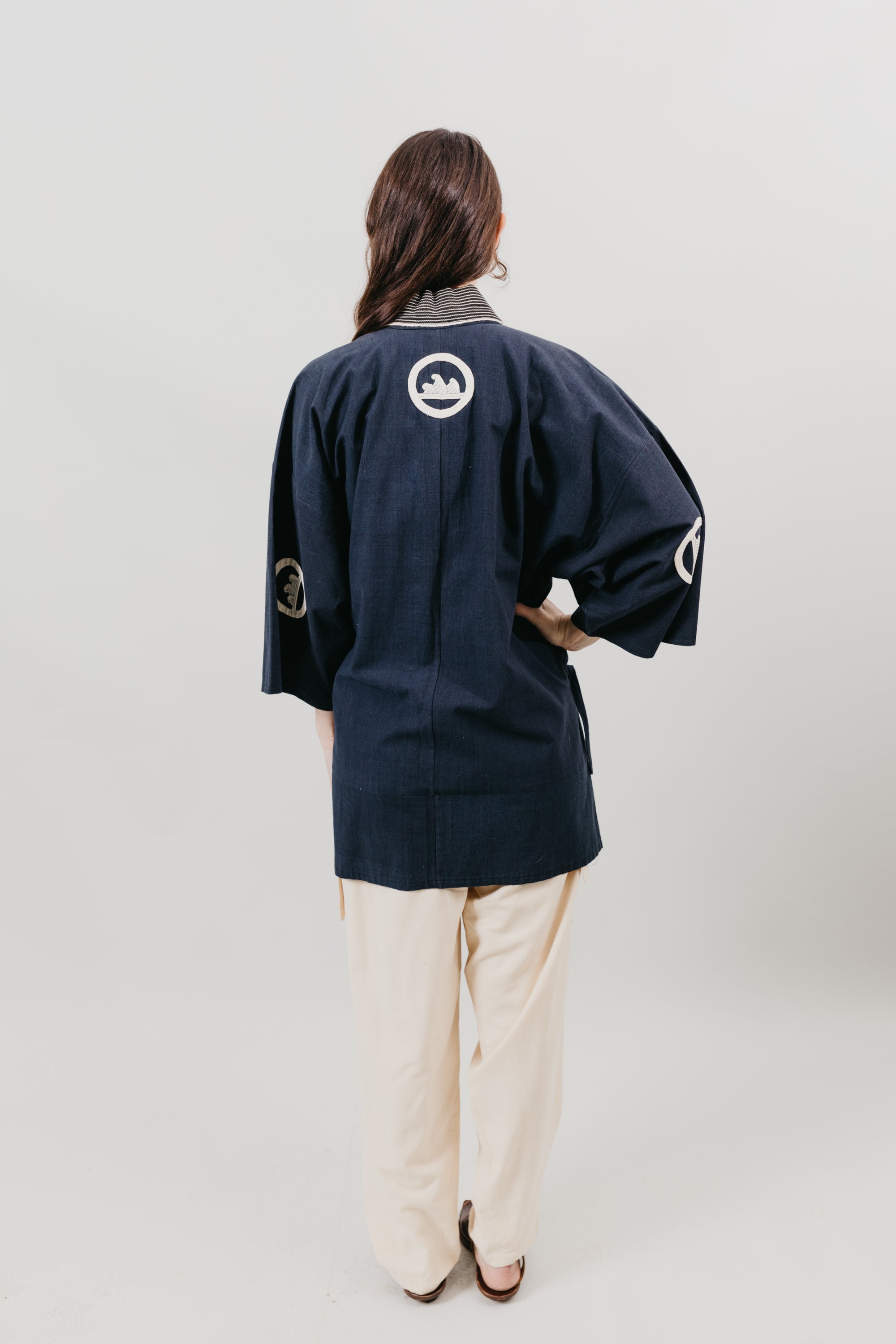 Japanese American woman in a navy Hippari and cream pants standing in front of a white background.