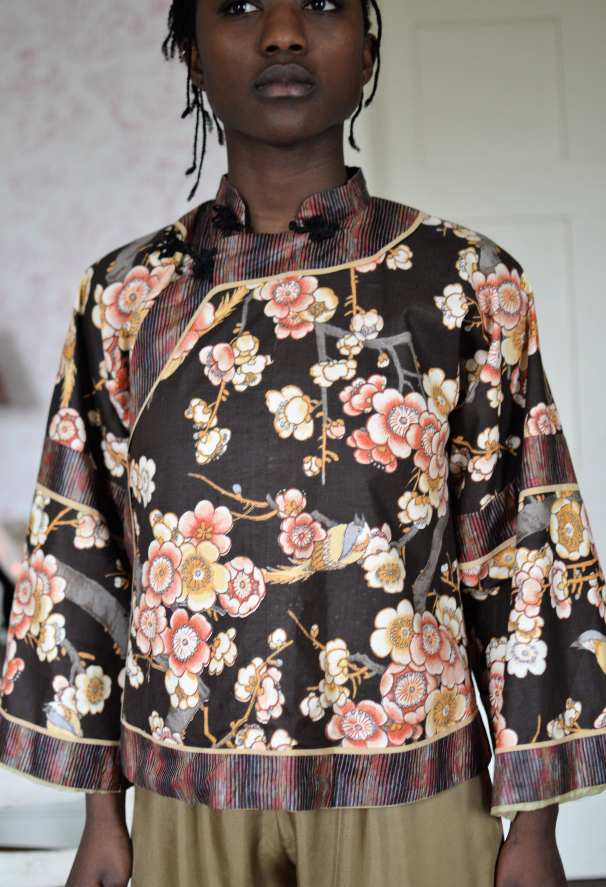 Black woman wearing a short, floral Chinese Jacket with striped facings. 