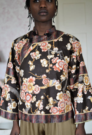 Black woman wearing a short, floral Chinese Jacket with striped facings. 