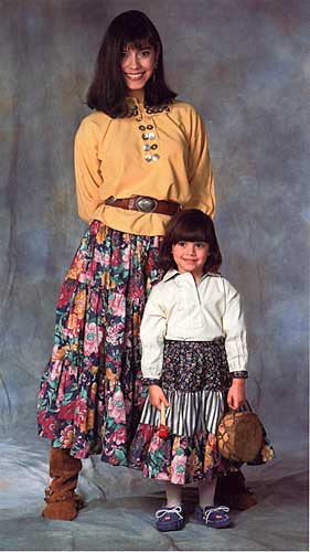 Woman and Child wearing 120 Navajo Blouse and Skirt. Child is standing in front of woman holding a small drum.
