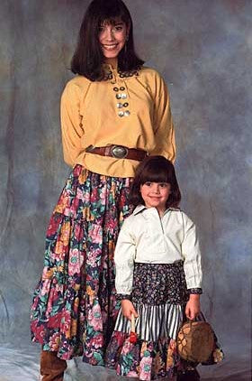 Woman and Child wearing 120 Navajo Blouse and Skirt.  Child is standing in front of woman holding a small drum.