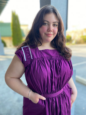 Close up of young woman wearing a purple sleeveless dress with some embellished shoulder yoke.